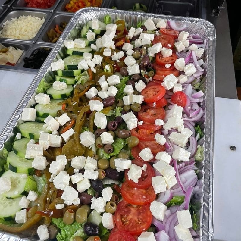 A large greek salad for a catering event with feta cheese, tomatoes, onions, cucumbers, olives, and peppers